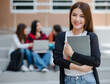 © Bangkok Click Studio - Close up young attractive female college students holding document files smiling at camera with blurry university campus and other students. Outdoor. Concept for education, college students life
