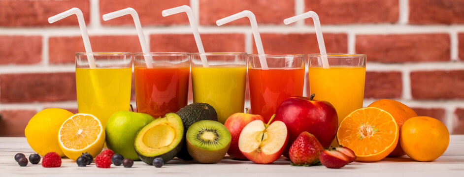Different fruits juice in glass, apple, orange and strawberry juice with straw, looking refreshing on colourful wood board in front of brick wall background. Picture decorating with fresh fruits