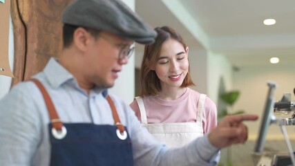 Wall Mural - Asian male coffee shop manager teaching young woman staff working on digital tablet. Small business cafe and restaurant owner instruct part time employee preparing service to customers before opening