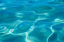 Turquoise Pure Clear Water In The Sea, Sun Glare, Waves And Sea Sand. Calm Sea Water Background