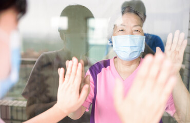 Wall Mural - Senior woman in medical mask communicates with her daughter through the window. Elderly quarantined, isolated. Pandemic coronavirus covid-19