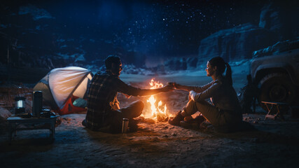 Wall Mural - Happy Couple Sitting by Campfire Sharing Cup of Drink, Watching Night Sky while Camping in the Canyon. Two Traveling Young people Tell Inspirational Stories about Life, Look at Milky Way Stars