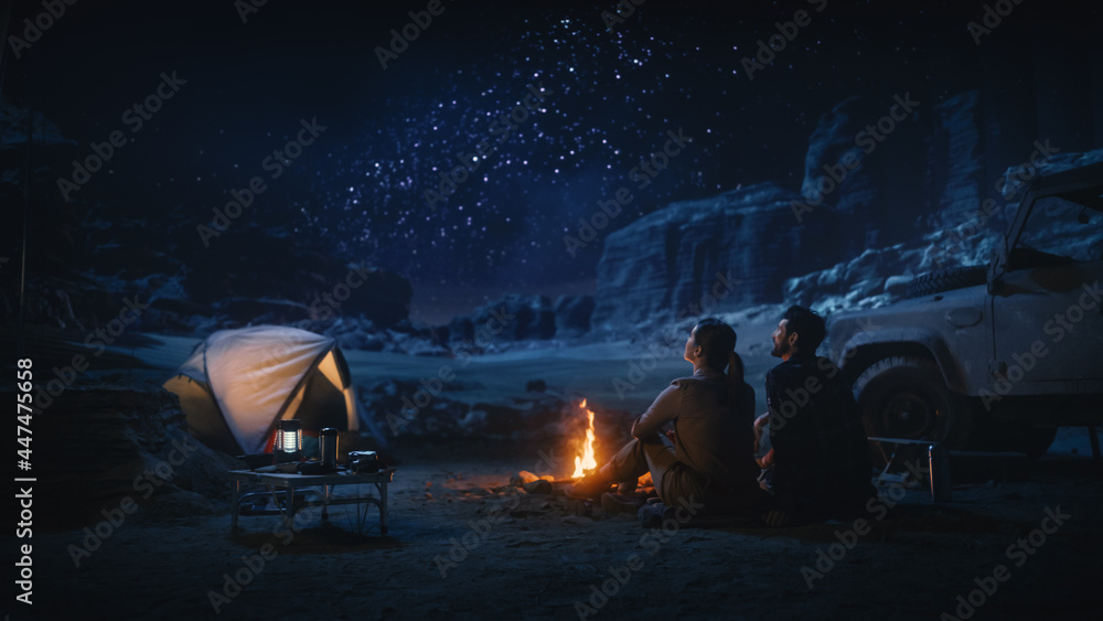Happy Couple Tent Camping in the Canyon, Sitting by Campfire Watching Night Sky with Milky Way Full of Bright Stars. Two Travelers In Love On a Romantic Vacation Trip. Back View Shot - obrazy, fototapety, plakaty 