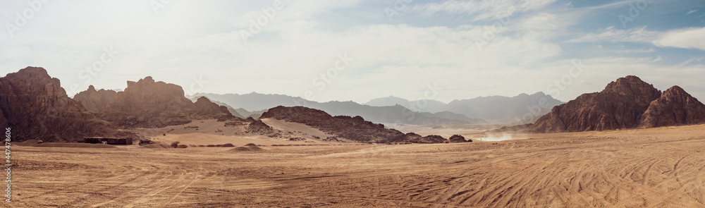 Safari and travel to Africa, extreme adventures or science expedition in a stone desert. Sahara desert at sunrise, mountain landscape with dust on skyline, hills and traces of the off-road car. - obrazy, fototapety, plakaty 