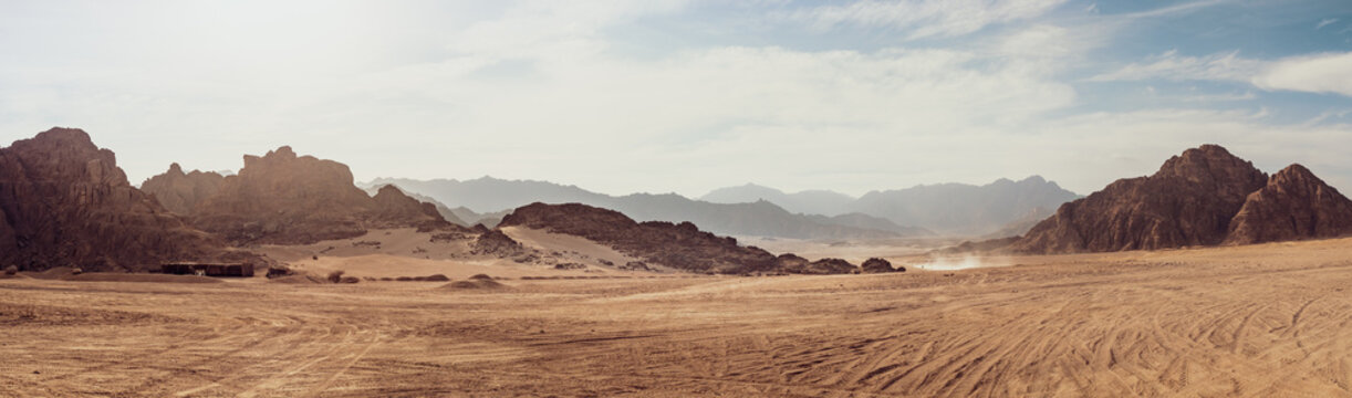 Safari and travel to Africa, extreme adventures or science expedition in a stone desert. Sahara desert at sunrise, mountain landscape with dust on skyline, hills and traces of the off-road car.