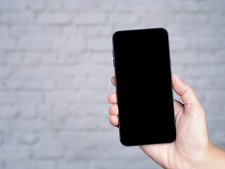 Wall Mural - hand holding of a smartphone with white brick wall background. close-up photo. space for text. techn