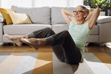 Happy Senior Woman Doing Sit-ups With Hands Behind Her Head In The Living Room