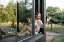 Young Woman Enjoy Of Resting At Modern House Or Hotel In Pine Forest, Sitting With Tablet On The Window Sill And Greeting Someone. Beautiful Destinations For Vacation