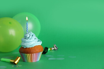 Wall Mural - Delicious birthday cupcake with candle near balloons and party blowers on green background, space for text