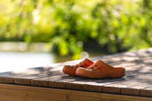 A Pair Of Orange Rubber Clogs On The Pier By The Lake, Close-up