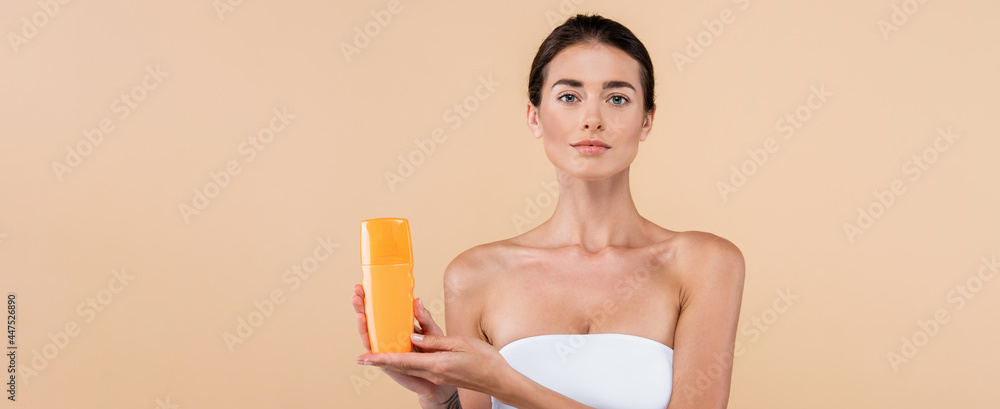 young woman in strapless top showing bottle of sunblock isolated on beige, banner - obrazy, fototapety, plakaty 