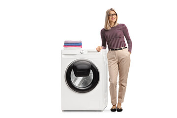 Wall Mural - Full length portrait of a young woman leaning on a washing machine with folded clothes on top