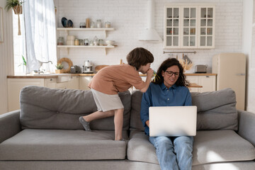 Wall Mural - Frustrated young woman, entrepreneur or remote worker work on laptop tired stressed of hyperactive disobedient little kid distract mom from business occupation in home office on sofa in living room