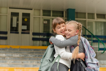 two cute happy girls schoolgirls with backpacks are playing near the school. High quality photo