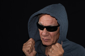 Wall Mural - Older man wearing a dark hoodie and shades against a black background