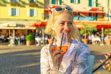 Woman tourist drinking a sunset cocktail by the lakefront in an open pub of Ascona historic city in Switzerland, in Ticino Canton on Lake Langensee.