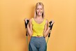 Beautiful blonde woman training arm resistance with elastic arm bands sticking tongue out happy with funny expression.