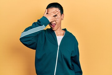 Sticker - Beautiful hispanic woman with short hair wearing sporty jacket peeking in shock covering face and eyes with hand, looking through fingers with embarrassed expression.