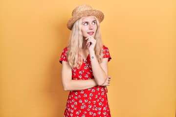 Canvas Print - Beautiful caucasian woman with blond hair wearing summer hat with hand on chin thinking about question, pensive expression. smiling with thoughtful face. doubt concept.