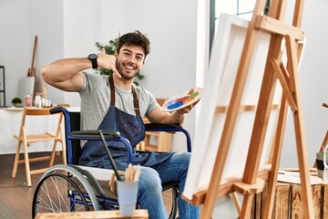 Sticker - Young hispanic man sitting on wheelchair painting at art studio smiling doing phone gesture with hand and fingers like talking on the telephone. communicating concepts.