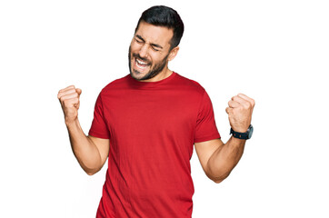 Wall Mural - Young hispanic man wearing casual clothes very happy and excited doing winner gesture with arms raised, smiling and screaming for success. celebration concept.