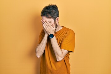 Wall Mural - Caucasian man with beard wearing casual yellow t shirt with sad expression covering face with hands while crying. depression concept.