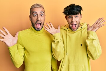 Poster - Homosexual gay couple standing together wearing yellow clothes celebrating crazy and amazed for success with arms raised and open eyes screaming excited. winner concept