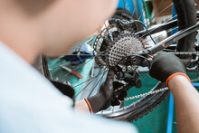 bicycle mechanic's hand with gloves uses an allen key to install the rear derailleur while working in a workshop