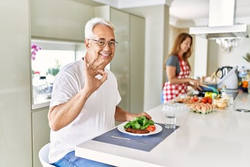 Wall Mural - Middle age hispanic couple eating healthy meal at home doing ok sign with fingers, smiling friendly gesturing excellent symbol