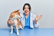 © Krakenimages.com - Beautiful hispanic veterinarian woman checking dog health celebrating victory with happy smile and winner expression with raised hands
