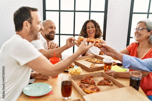 Group of middle age people smiling happy eating italian pizza sitting on the table at home