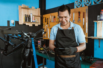 Portrait of a repairman in an apron using a cellphone while repairing a bicycle in a bicycle repair shop