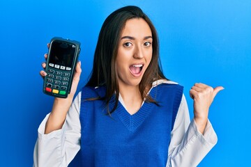 Sticker - Young hispanic girl holding dataphone pointing thumb up to the side smiling happy with open mouth