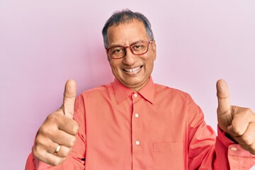 Sticker - Middle age indian man wearing casual clothes and glasses approving doing positive gesture with hand, thumbs up smiling and happy for success. winner gesture.