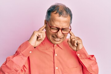 Poster - Middle age indian man wearing casual clothes and glasses covering ears with fingers with annoyed expression for the noise of loud music. deaf concept.