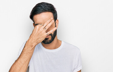 Wall Mural - Young hispanic man wearing casual white t shirt tired rubbing nose and eyes feeling fatigue and headache. stress and frustration concept.