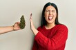 Beautiful brunette woman saying no to marijuana herb sticking tongue out happy with funny expression.
