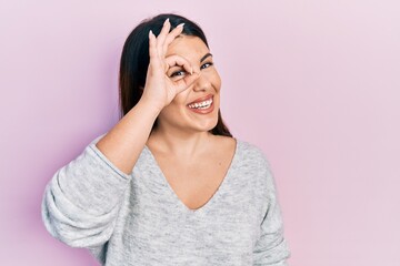 Sticker - Young hispanic woman wearing casual clothes doing ok gesture with hand smiling, eye looking through fingers with happy face.