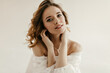 © Look! - Young lady with wavy hair and tender makeup in white modern shirt looking into camera on isolated background. Photo of girl in light clothes..