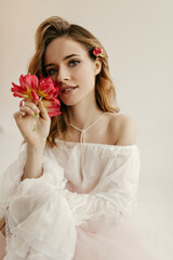 Wall Mural - Photo of charming lady with curly blond hair in white shirt with long sleeves holding red tulips on isolated background..