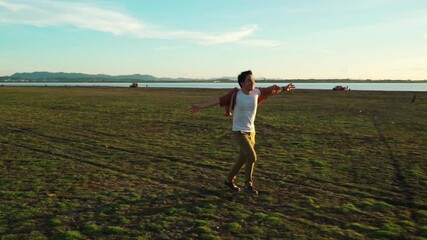 Wall Mural - slow-motion of cheerful man running with arms raised across the green field with sunlight

