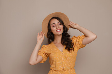 Wall Mural - Beautiful young woman with straw hat on beige background