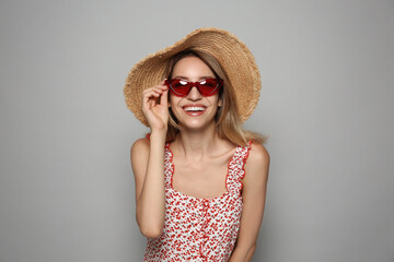 Poster - Beautiful young woman wearing straw hat and sunglasses on light grey background. Stylish headdress