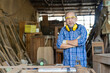 © amorn - Portrait of Asian senior male carpenter worker wearing safety goggles and earmuffs at work. Asian male woodworker. Asian male craftsman
