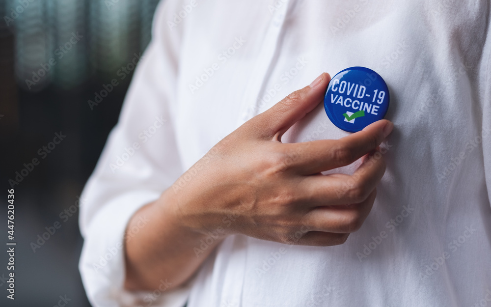 Closeup image of a woman putting Covid-19 vaccinated sign brooch on shirt - obrazy, fototapety, plakaty 