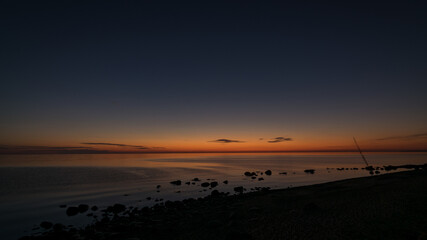 Wall Mural - orange sunset by the sea, dark stone silhouettes in the foreground, summer