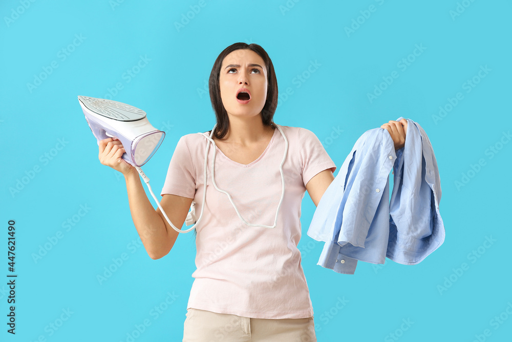 Upset young woman with iron on color background
