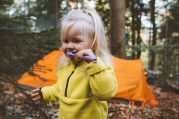 Child brushing teeth outdoor travel family camping vacation in forest toddler girl 2 years old with toothbrush dental care hygiene concept