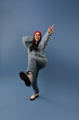© Look! - Positive long dark haired lady with red hat and glasses in trendy sweater, blue jeans and light cool boots raising her leg and arm..