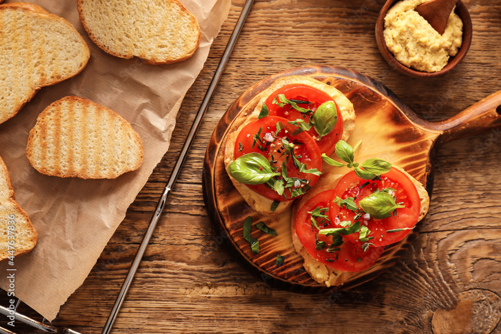 Tasty bruschettas with tomato and hummus on wooden background